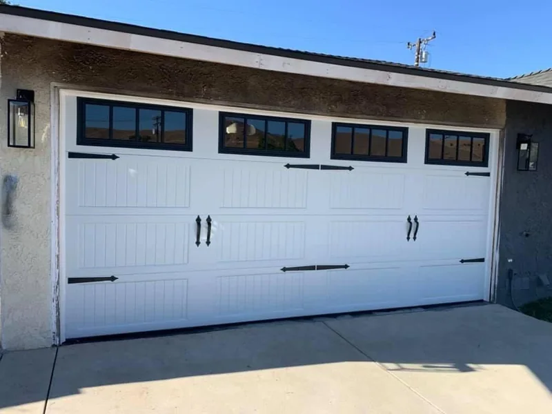 White carriage-style garage door with dark window frames and decorative hardware.
