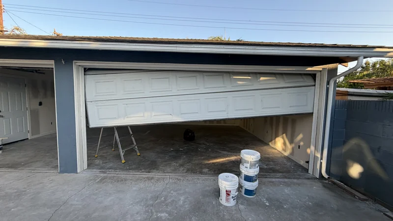 Before the repair: a white garage door sitting uneven and partly raised in its opening.