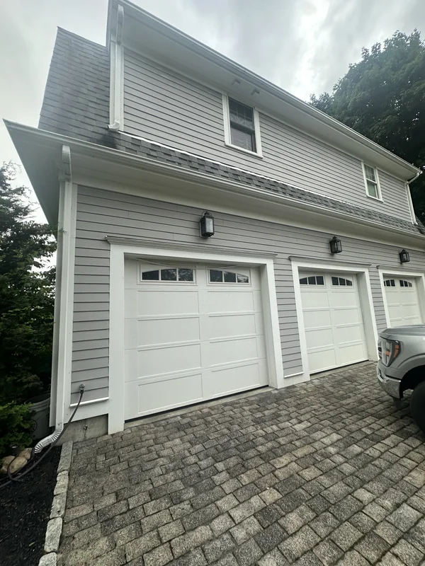 Three white carriage-style garage doors beneath gray siding.