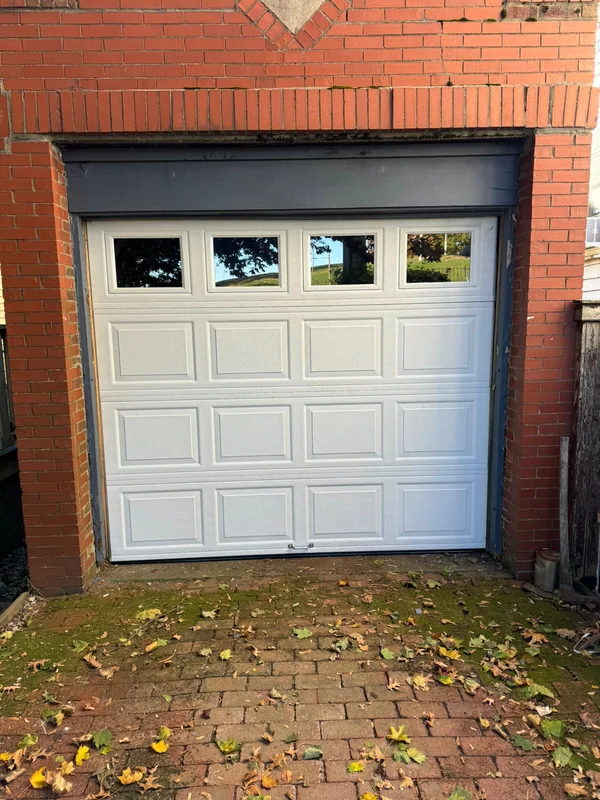Single white garage door with four windows set into a red-brick opening.