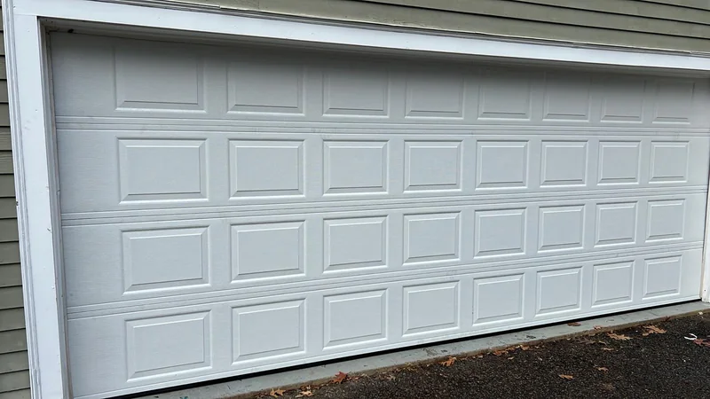 Wide white raised-panel garage door beneath horizontal siding.