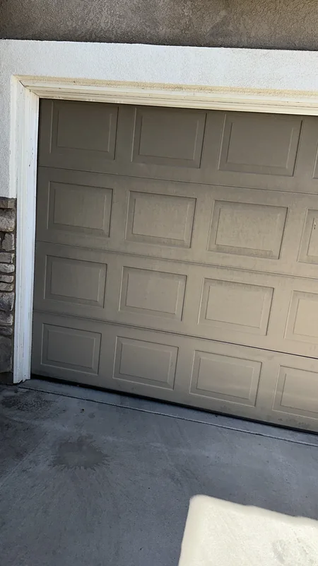 Angled detail of a taupe raised-panel garage door and its lower edge.